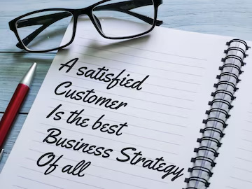 A notebook with A Satisfied customer is the best business strategy of all written on it.